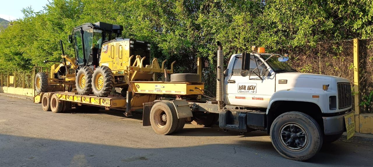 Un camión blanco transporta un tractor amarillo en un remolque.