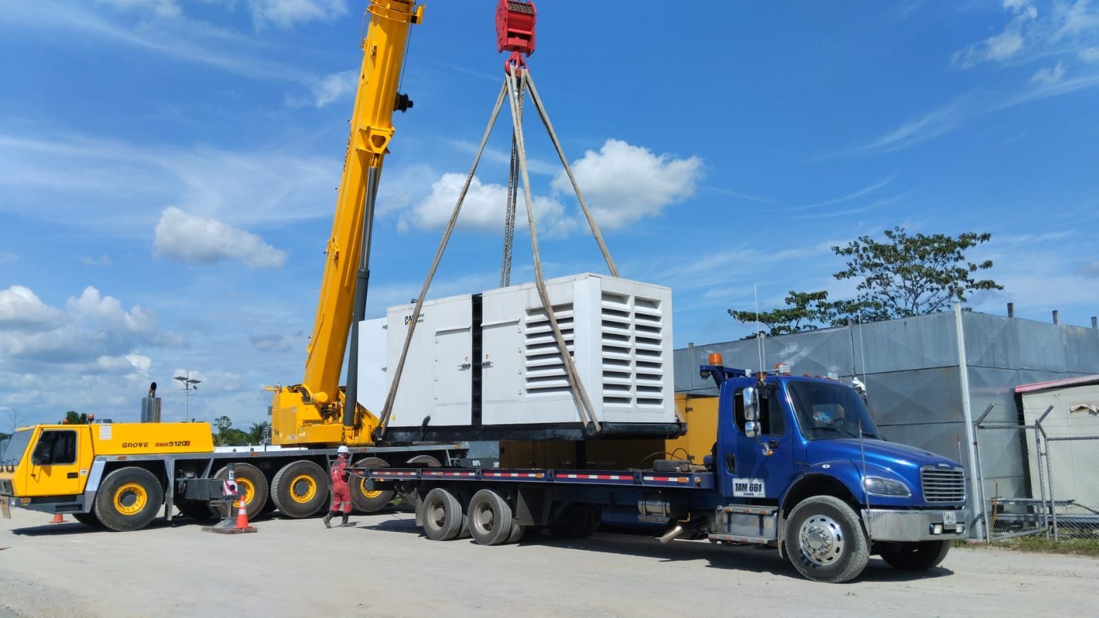 Una grúa amarilla está levantando una caja blanca en un camión de plataforma