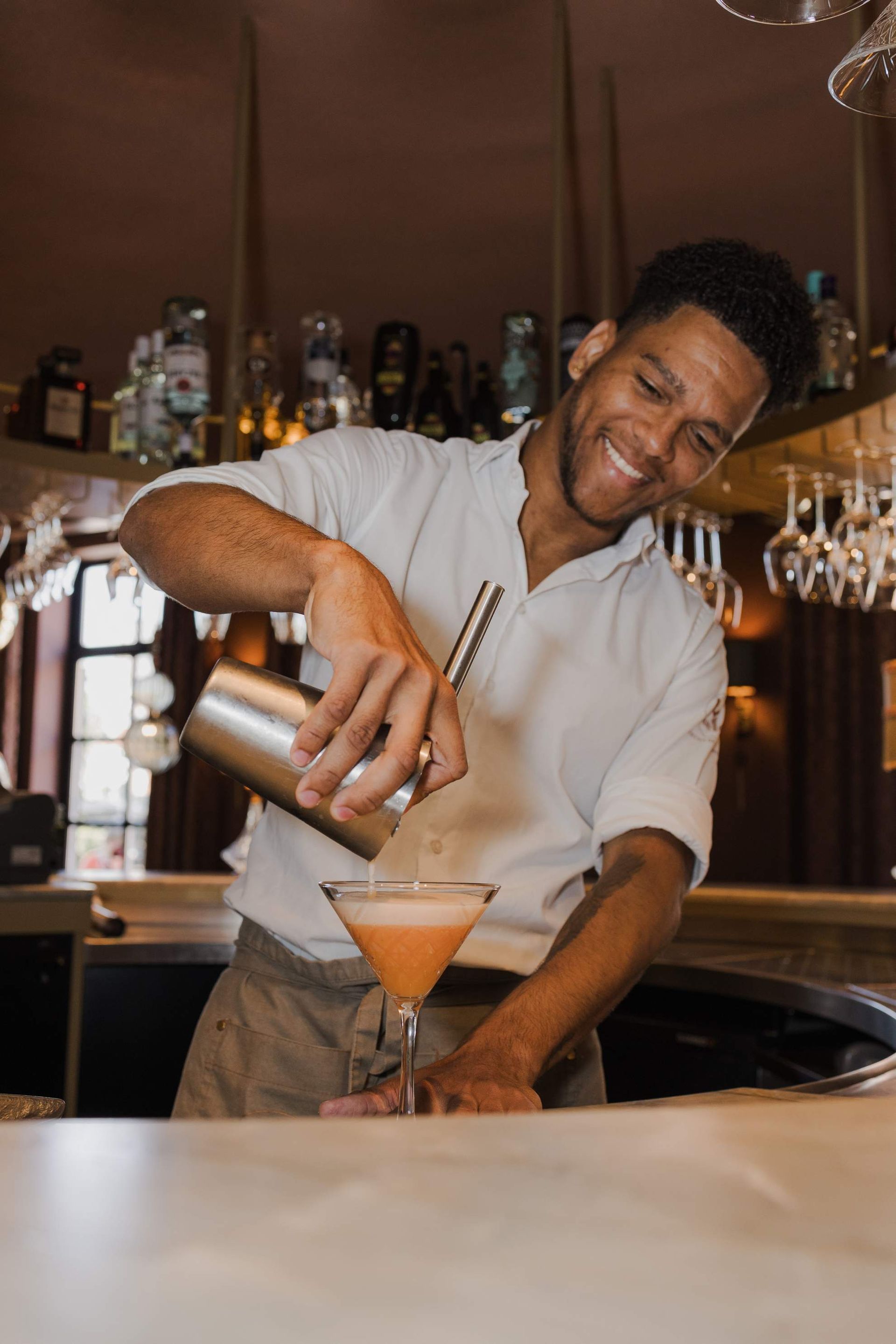Een barman schenkt met een glimlach een cocktail uit een shaker in een martiniglas.