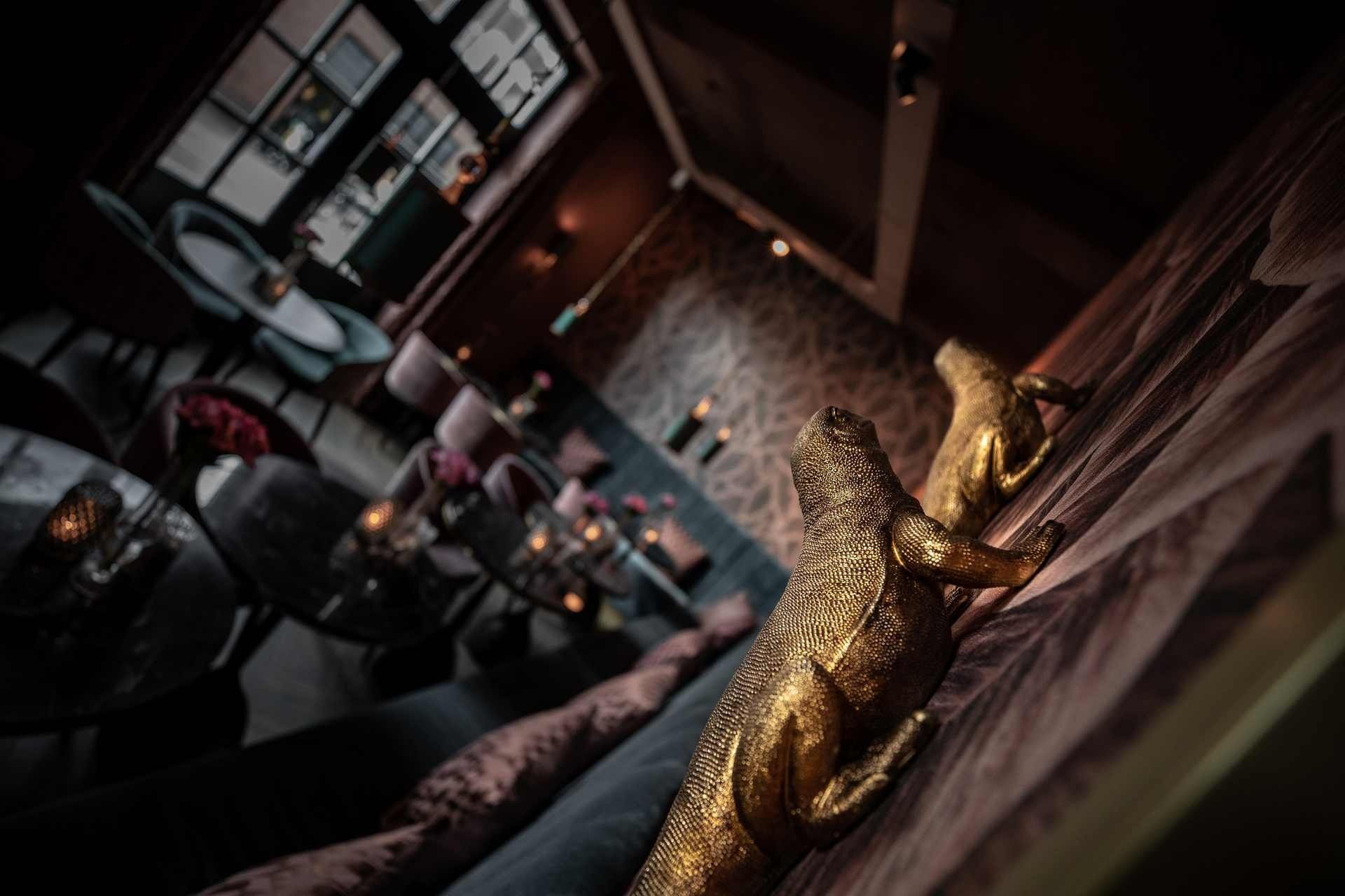 In een schemerig verlichte bar hangen twee gouden dinosaurussculpturen aan de muur.