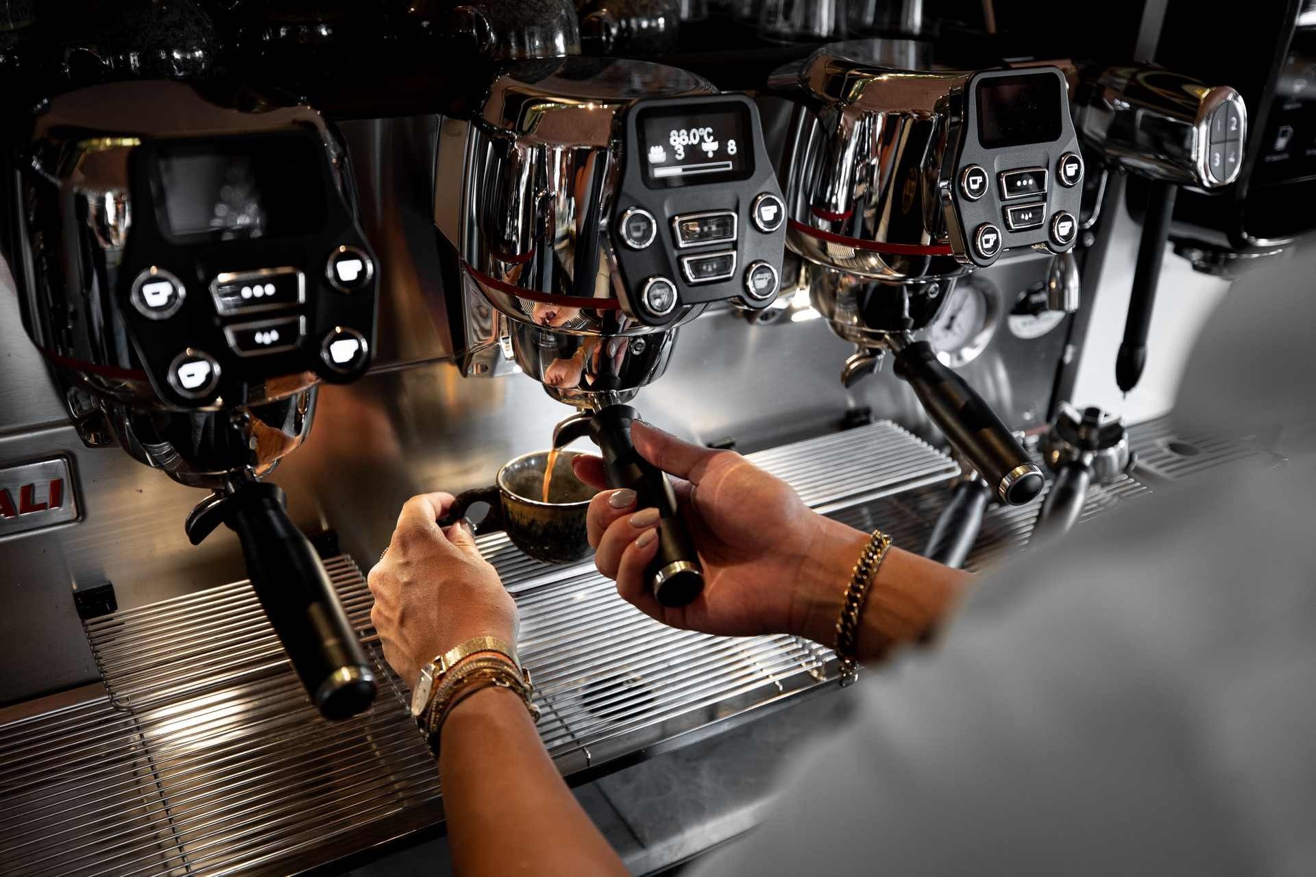Barista maakt espresso met drie verchroomde espressomachines.