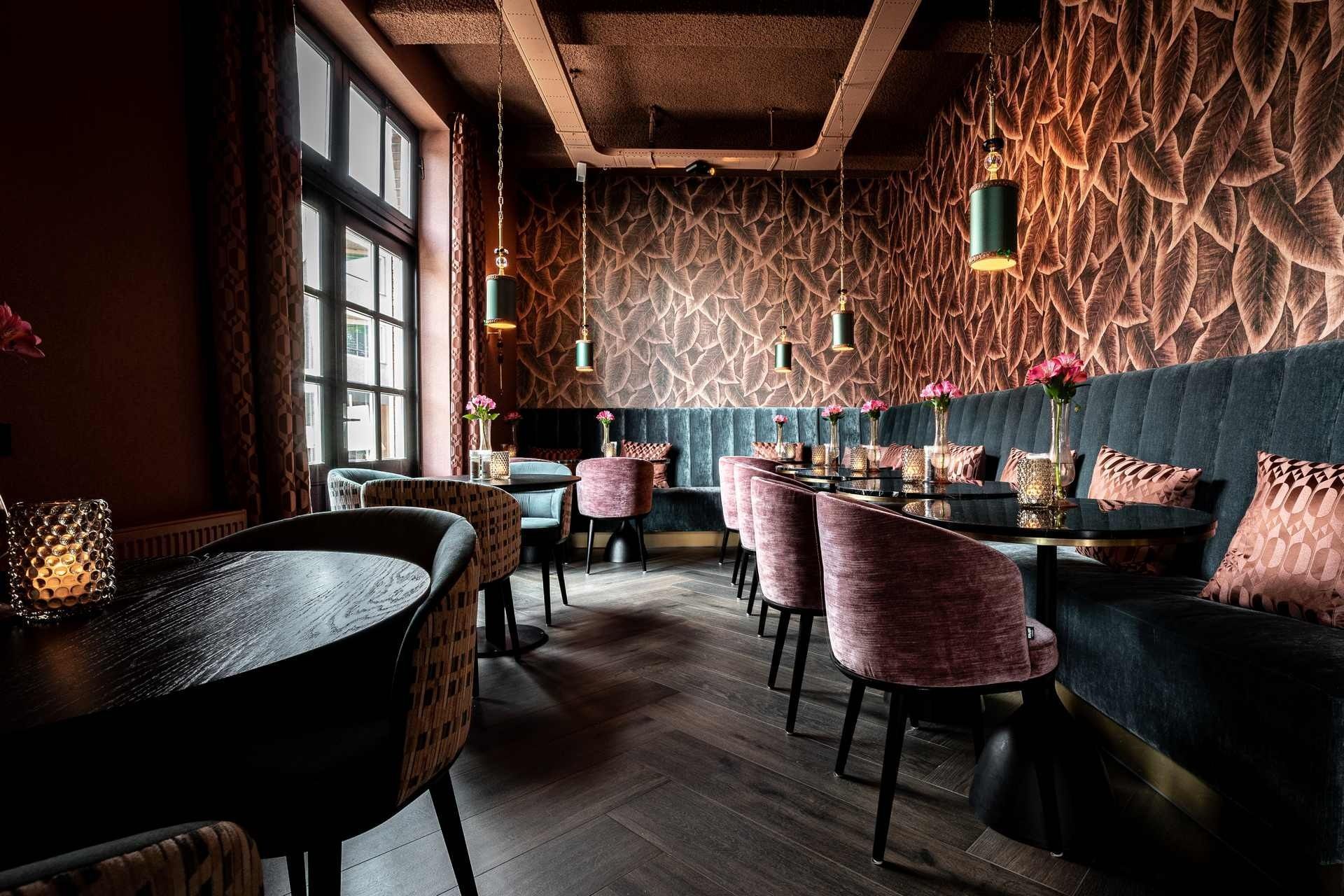 Elegant restaurantinterieur met donkere houten vloeren, fluwelen stoelen en behang met een patroon.