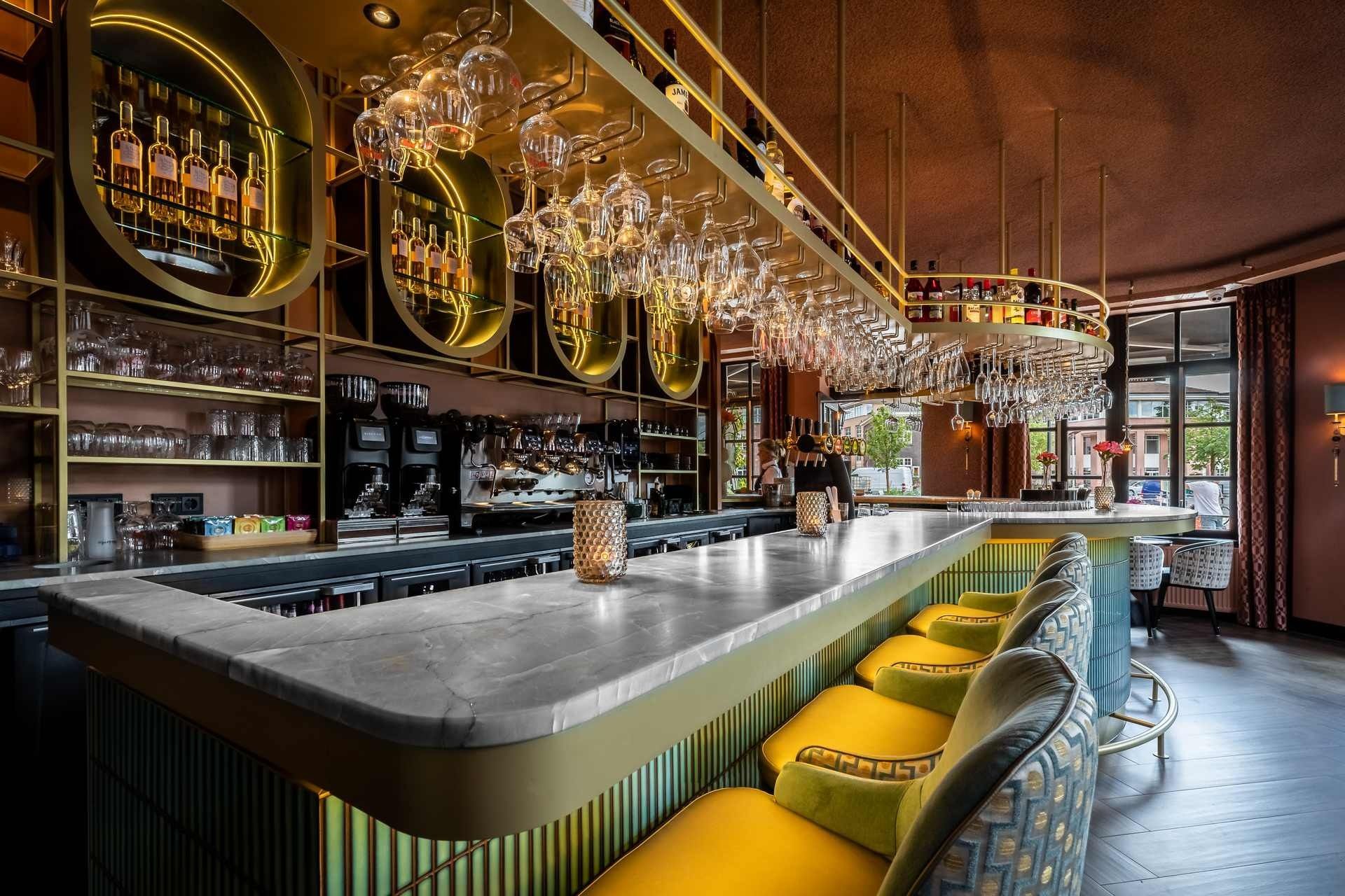 Stijlvol barinterieur met een marmeren aanrechtblad, gouden accenten en gele zitmeubels.