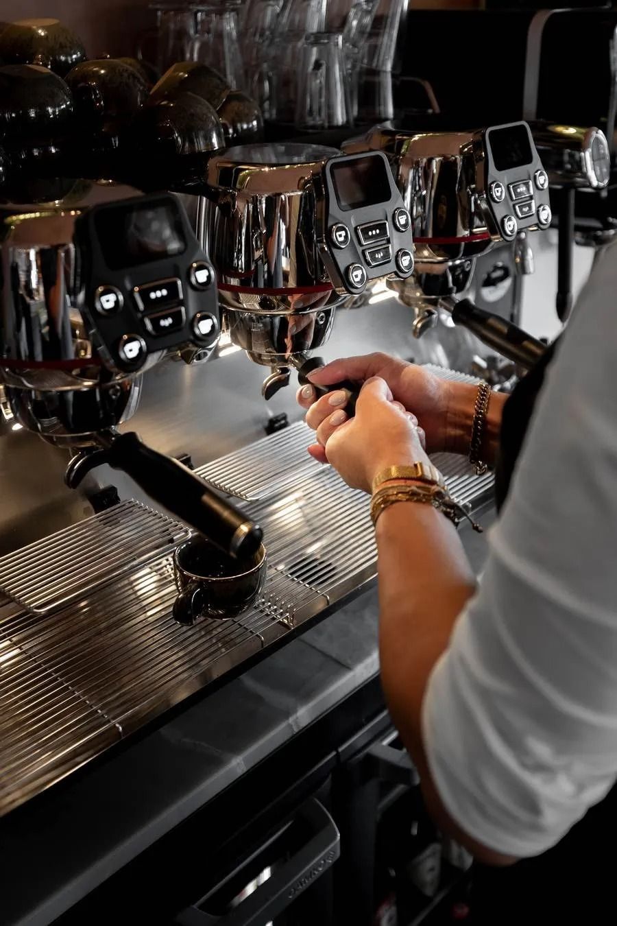 Barista bedient een espressomachine, met geconcentreerde handen. Roestvrij staal, zwarte handgreep, felle verlichting.