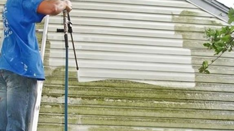 Person pressure washing a house siding, cleaning off green algae.