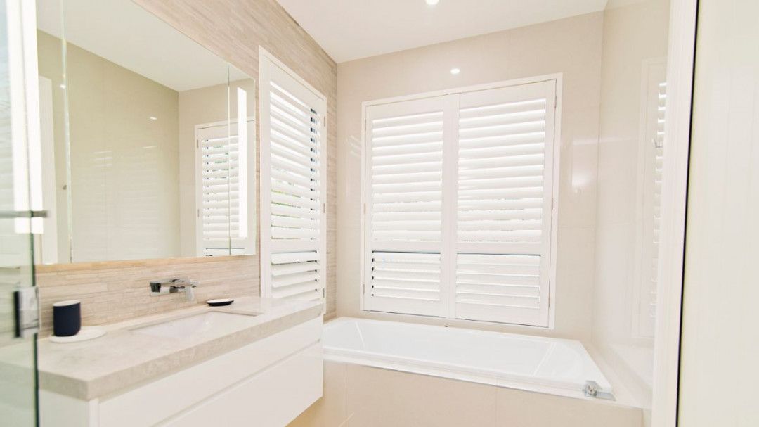 A bathroom with a tub , sink , mirror and shutters