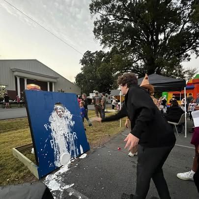 A woman is standing in front of a painting of a man covered in foam.
