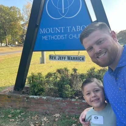 A man and a boy are posing for a picture in front of a mount tabor methodist church sign.
