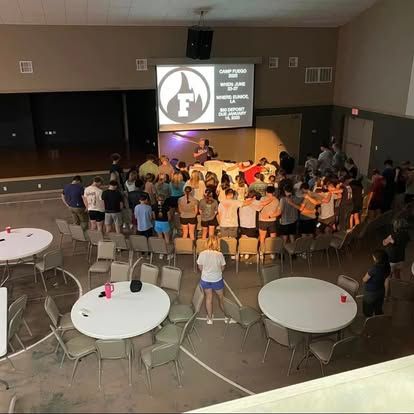 A large group of people are standing in a room with tables and chairs.