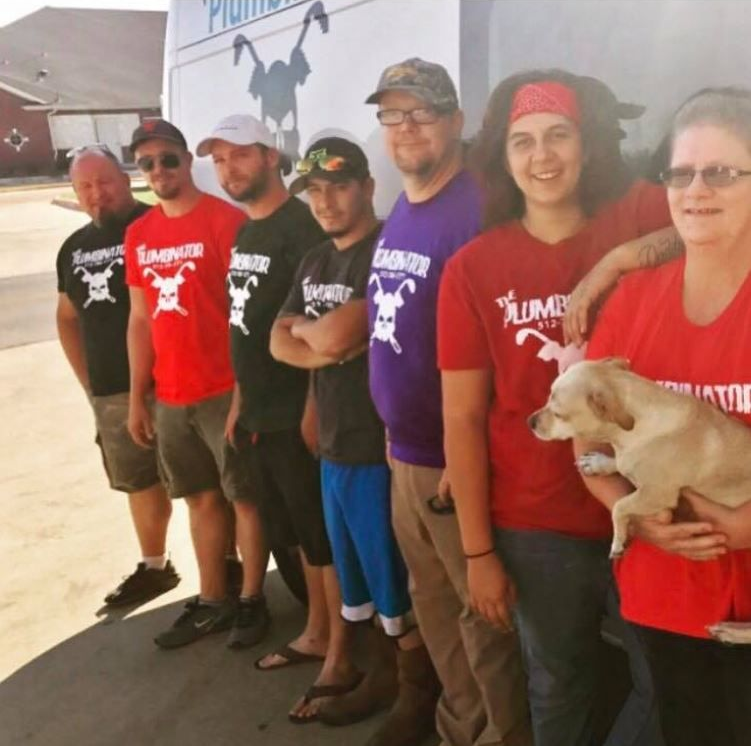 A line of seven people wearing matching team shirts with a skull logo, standing outdoors, one person holding a small dog.