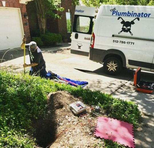 Three construction workers in a dirt trench outdoors, working on utility repairs next to a parked truck.