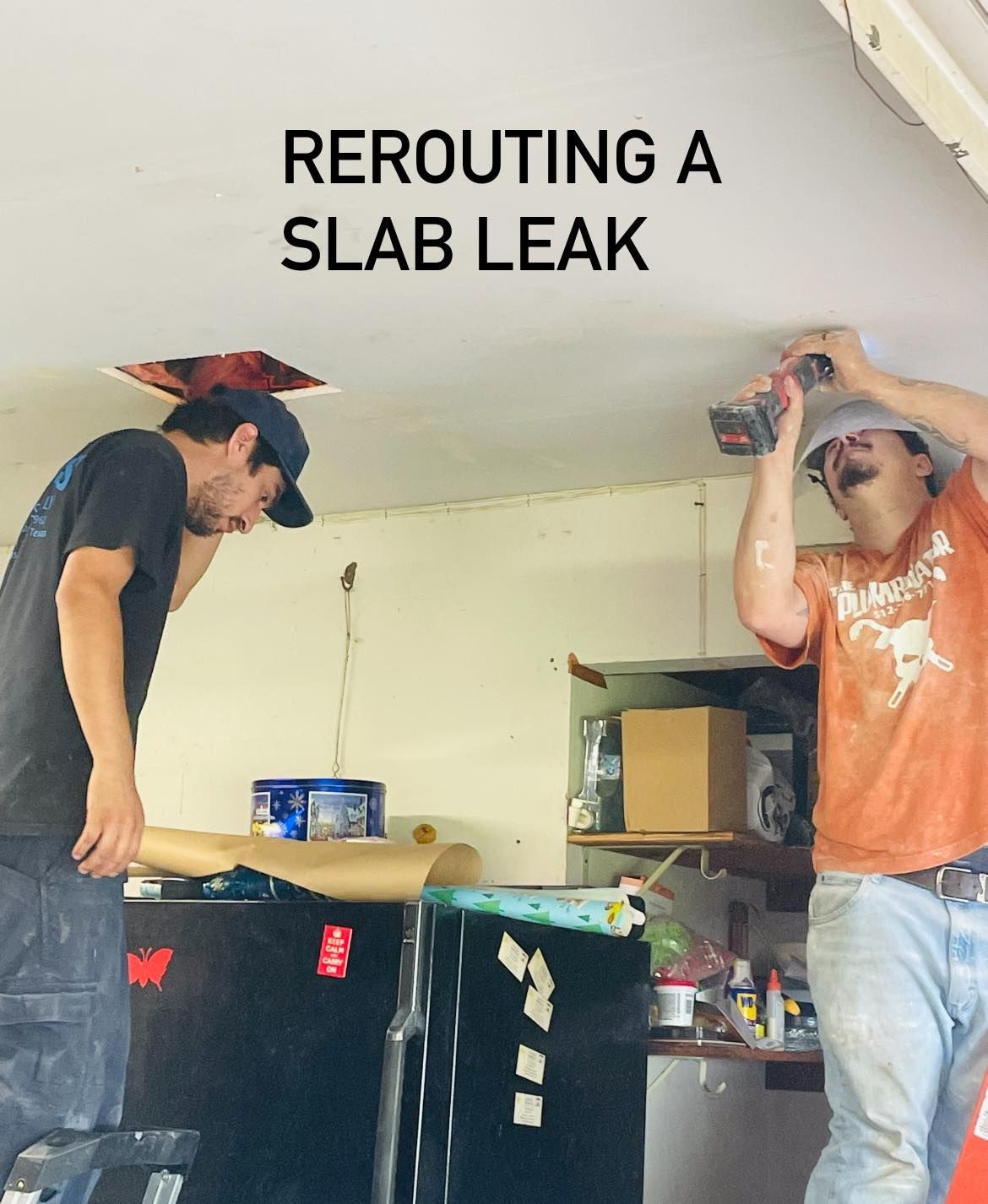 Two people in a crawlspace under a home, one in a red shirt and one in camouflage, installing white PVC plumbing pipes.