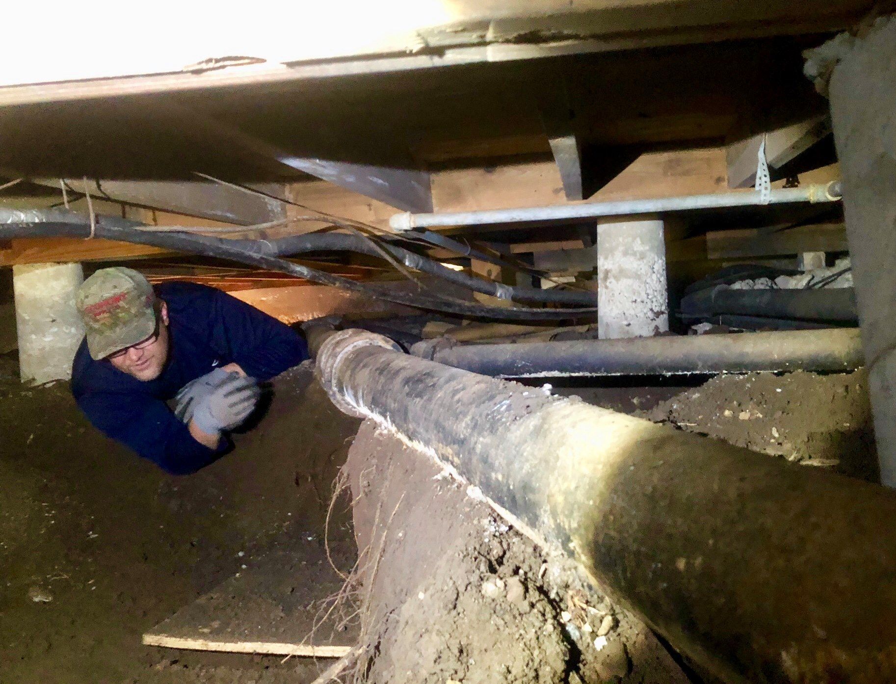 A level resting on a grey pipe installed in a narrow trench next to concrete, with tools and a person's legs nearby.