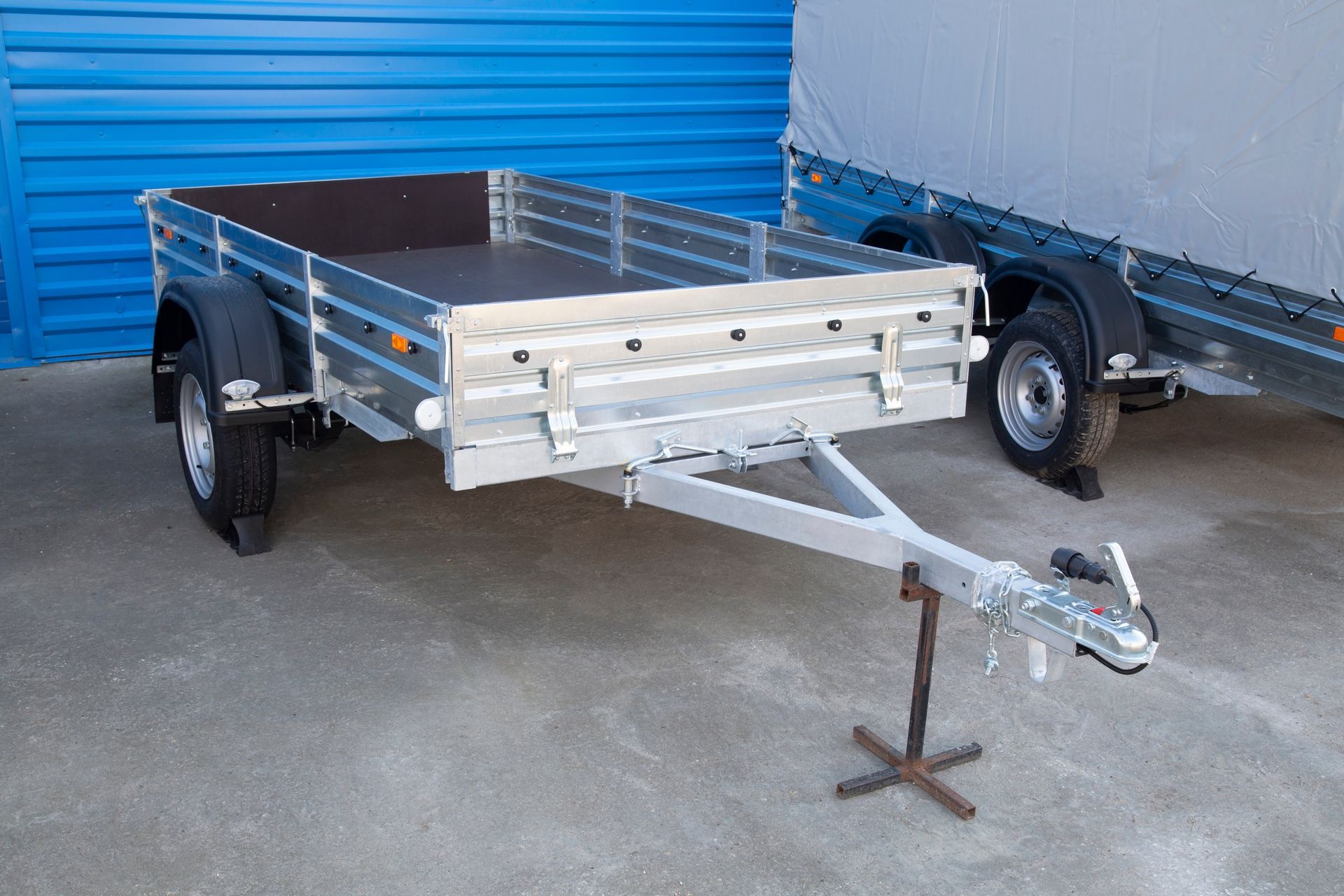 An open car trailer parked outdoors next to a cargo truck. An open car trailer parked outdoors next to a cargo truck.