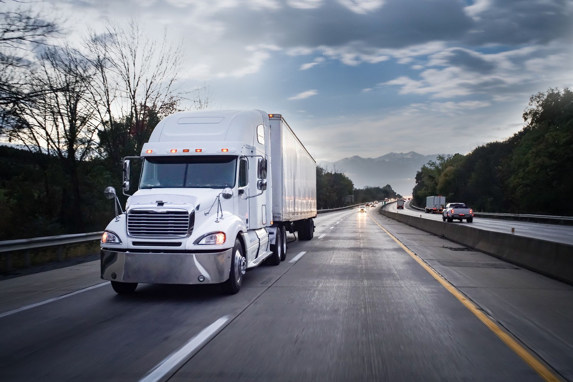 White semi truck driving on highway delivering freight on an open road at sunrise.