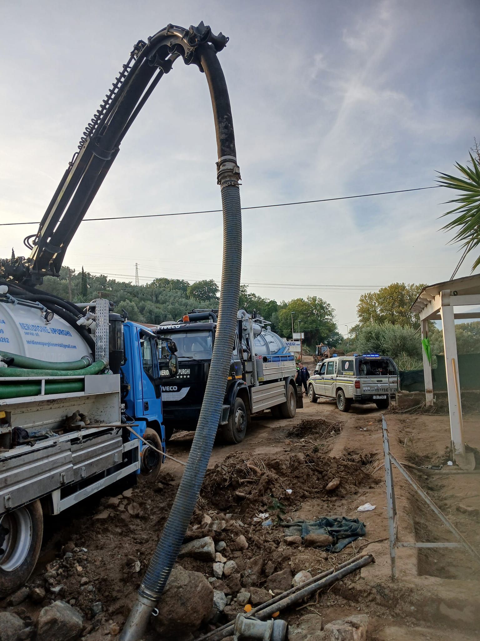 Tre autocisterne con grandi tubi flessibili che servono una strada sterrata.