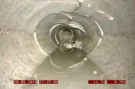 Una ripresa della telecamera all'interno di un tubo di cemento mostra acqua e danni, con una crepa vicino alla sommità.