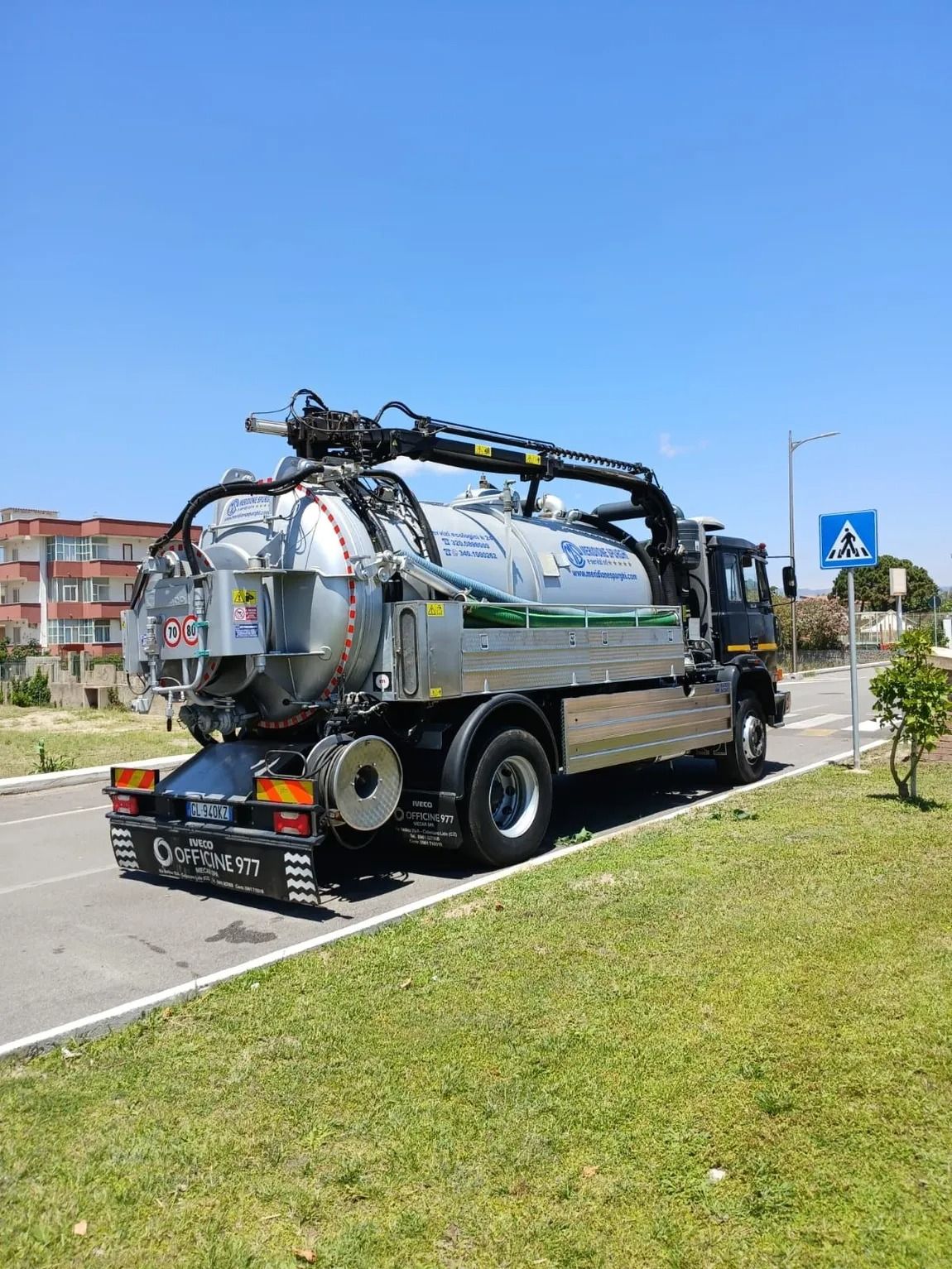 Un camion settico argentato parcheggiato su una strada, sotto un cielo azzurro.