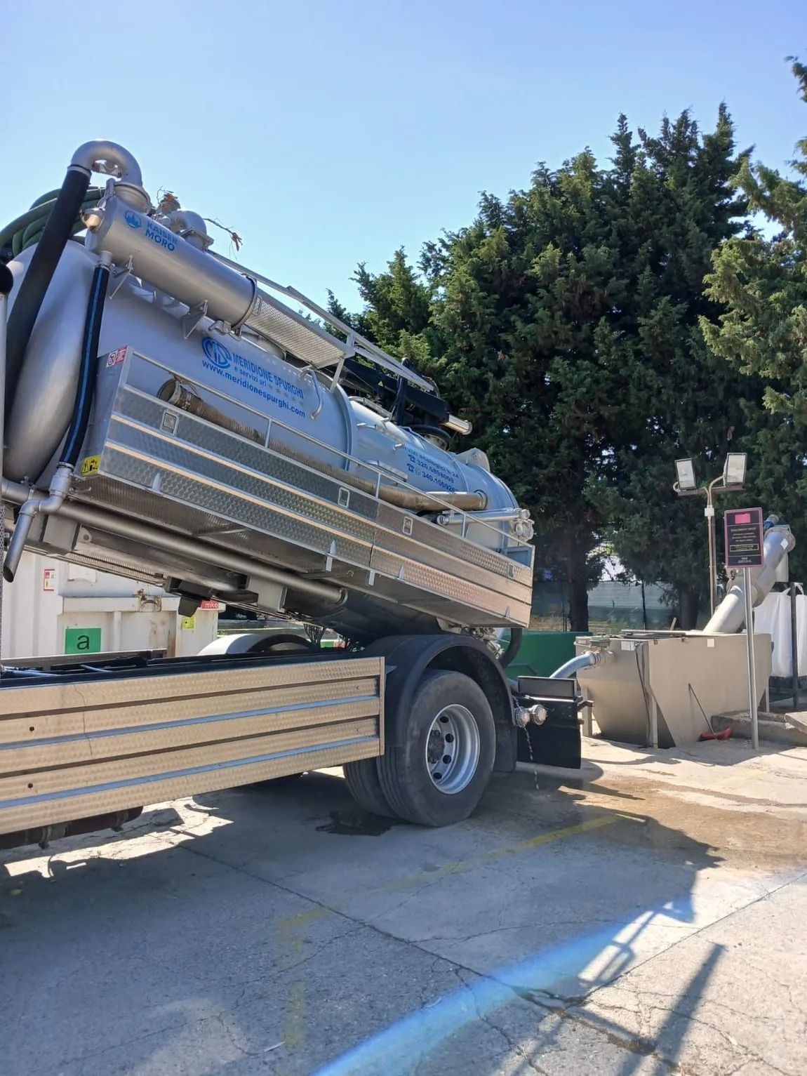 Un camion scarica il contenuto in una macchina, all'aperto, contro un cielo azzurro.