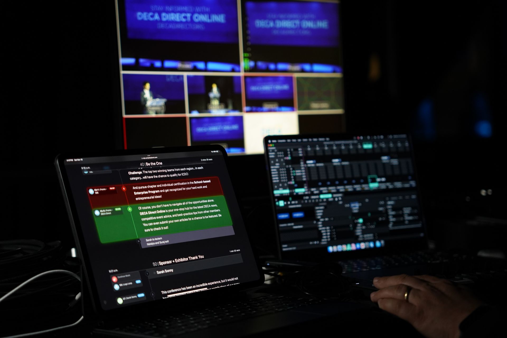 Control room: Laptops displaying live video feed and control panels, dark setting.