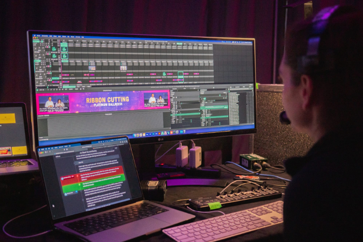 Person editing video on computer monitors. Editing software timeline visible.