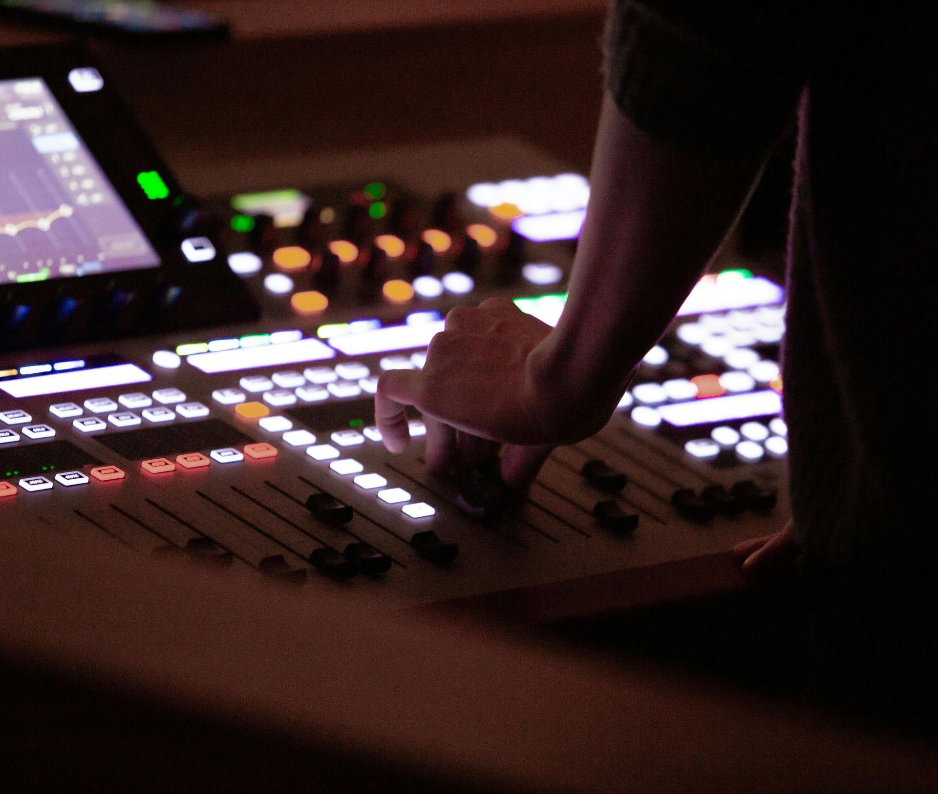 Person's hand adjusting sliders on a lit mixing console, likely in a recording studio.