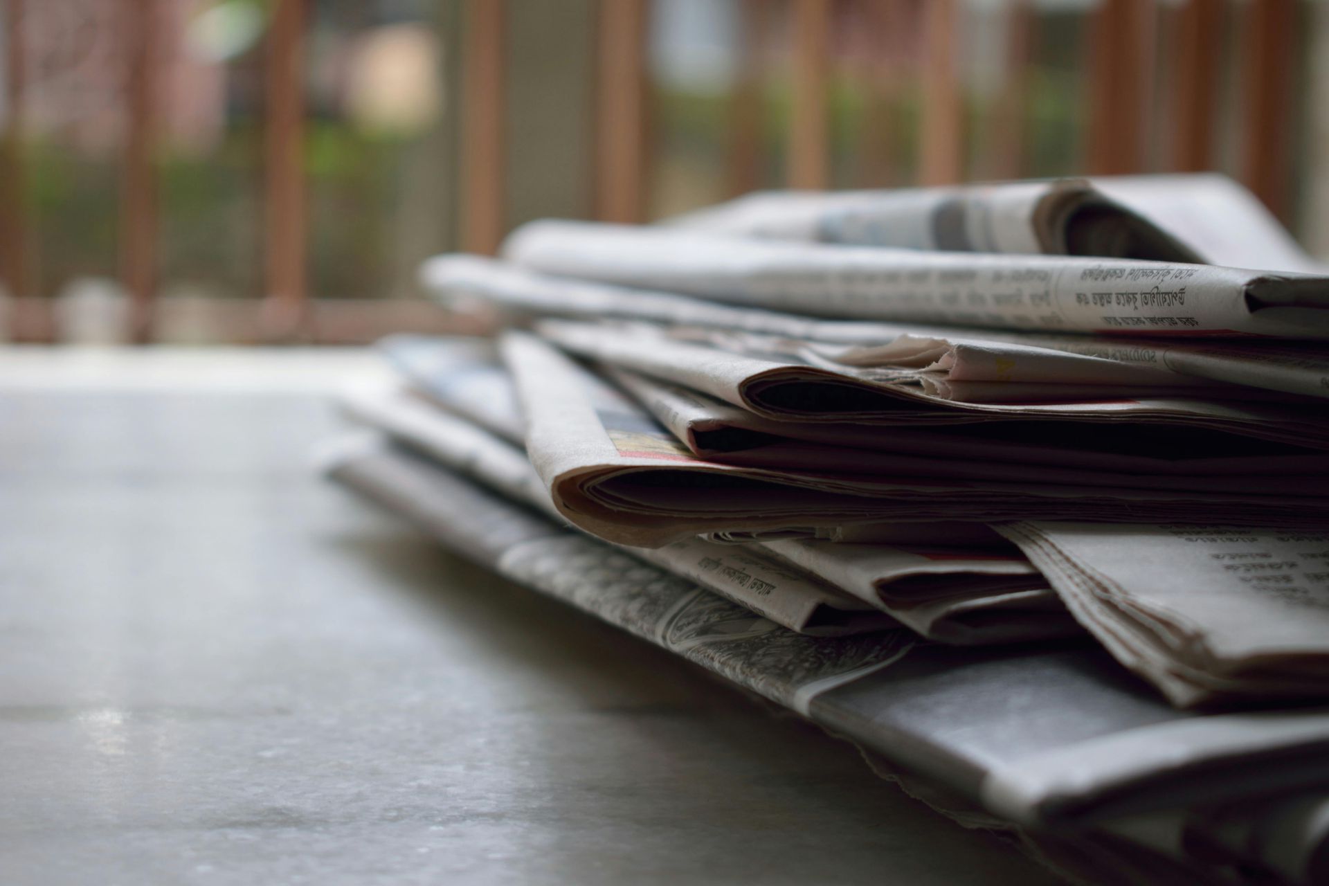 Pile of newspapers on a white surface with a blurred balcony background.