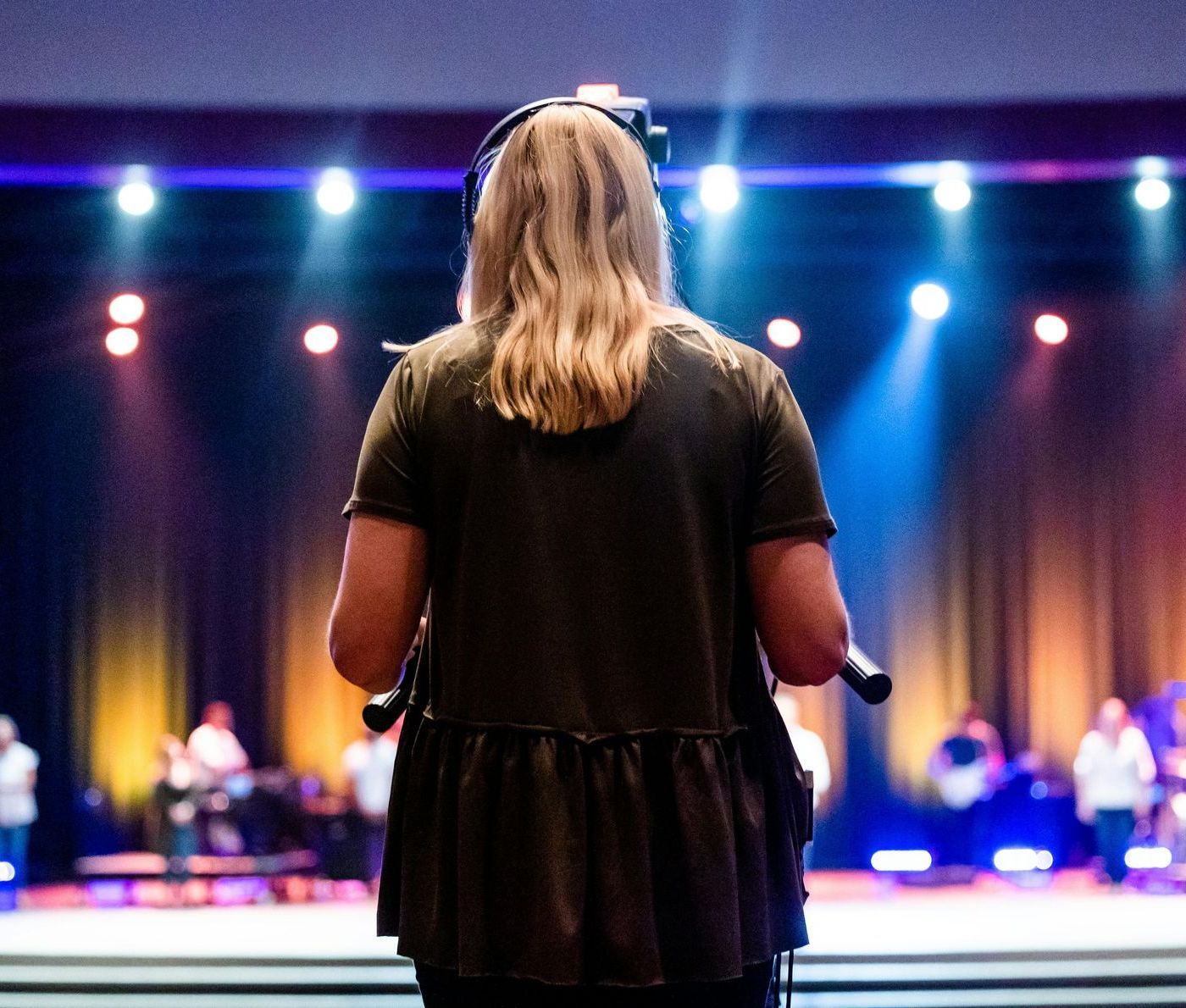 A woman or video technician is wearing a headset is filming an event on stage
