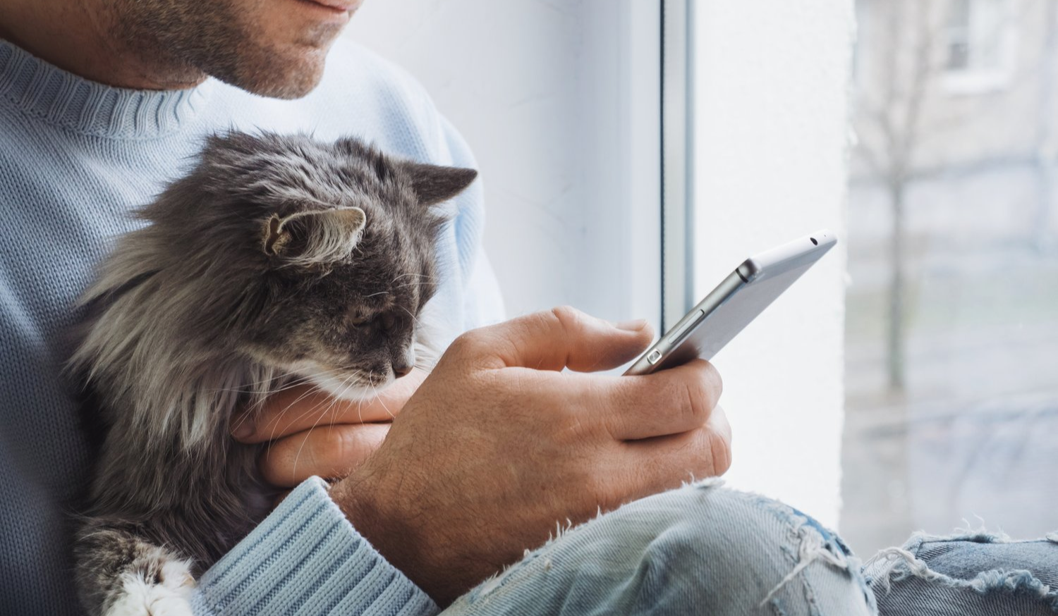 a man is holding a cat while using a cell phone .