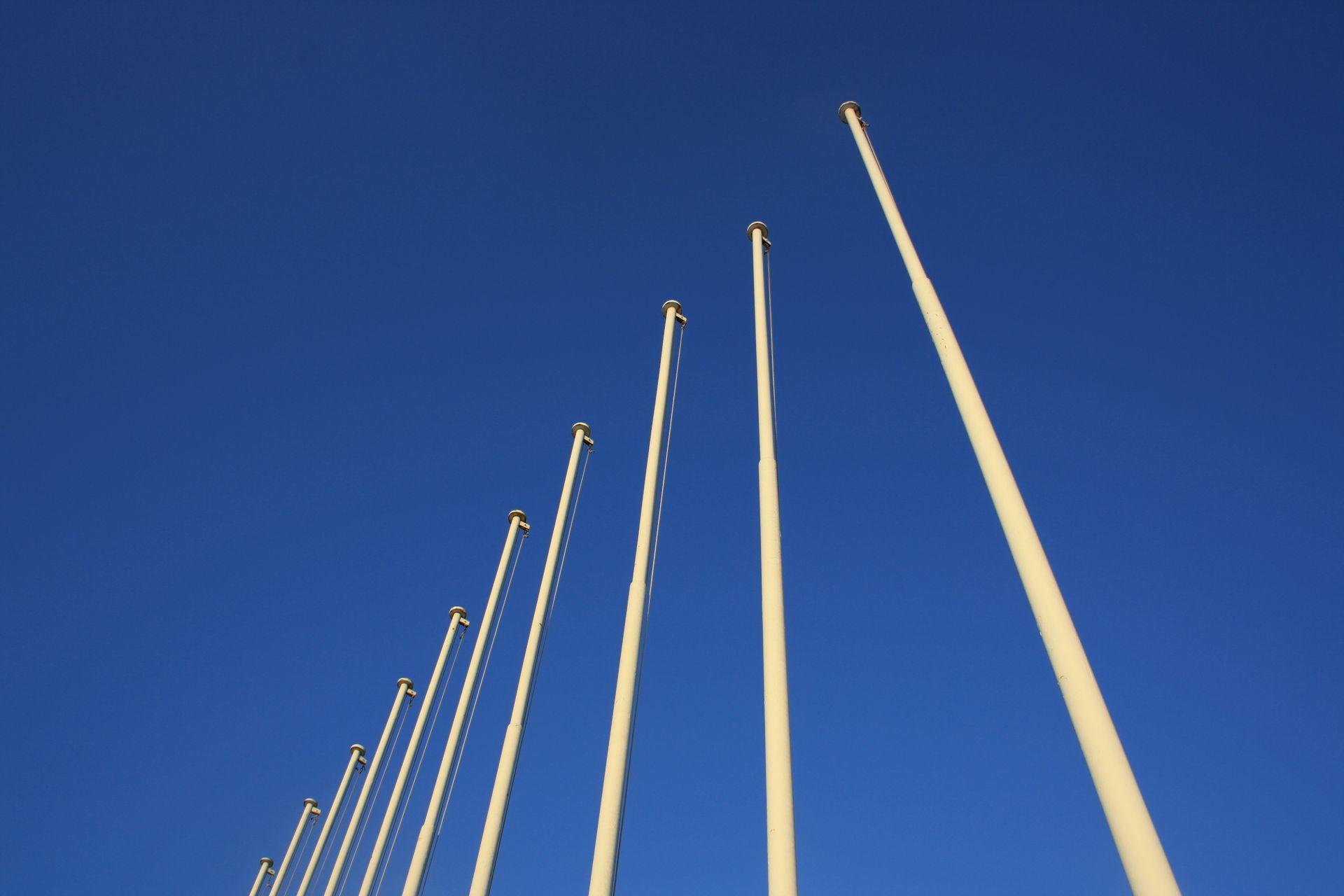 Tall empty flagpoles rising into a clear blue sky in an open outdoor area.