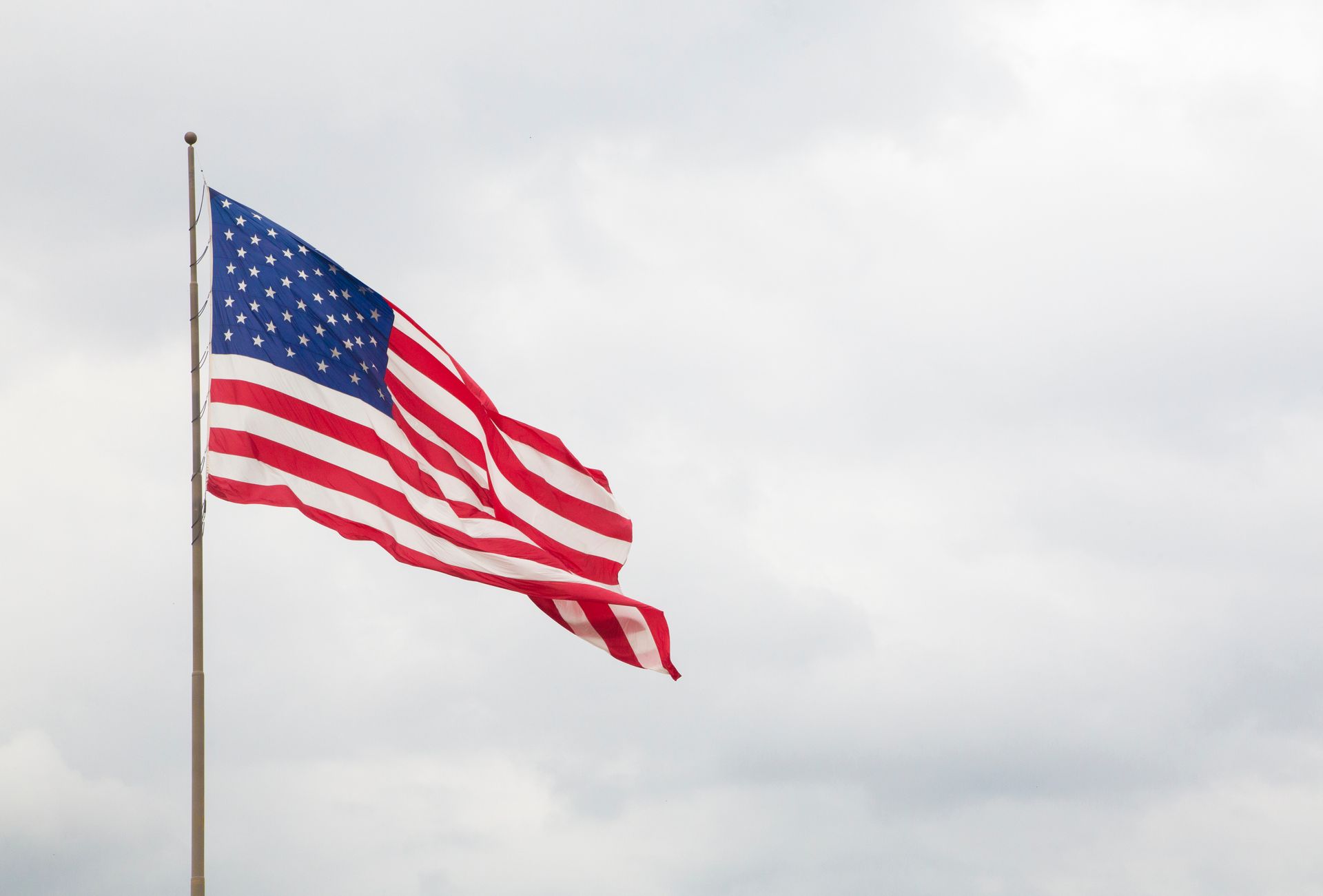 American flag waving on a tall flagpole against a cloudy sky outdoors.