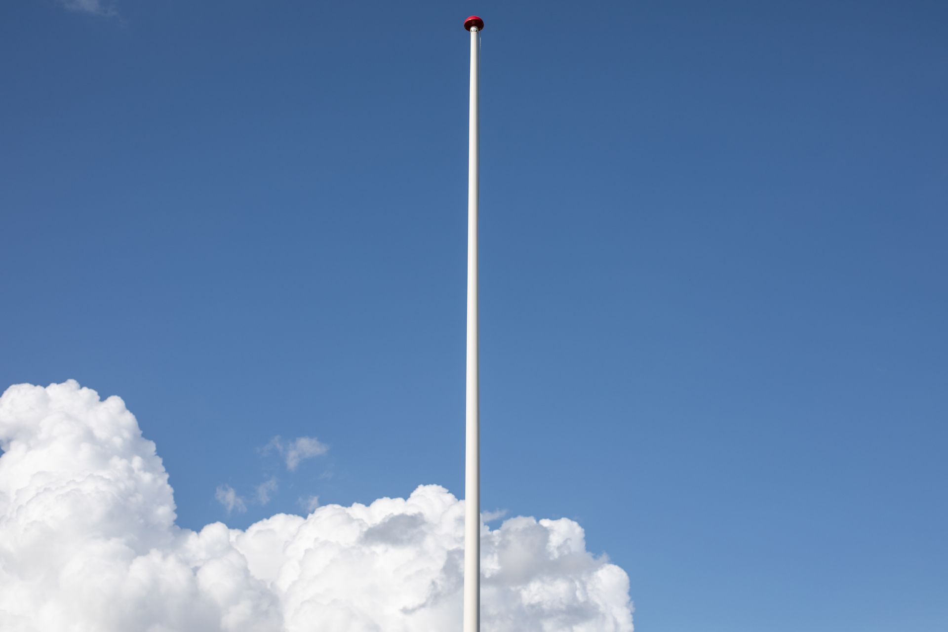 Tall white flag poles against clear blue sky with fluffy white clouds in background.