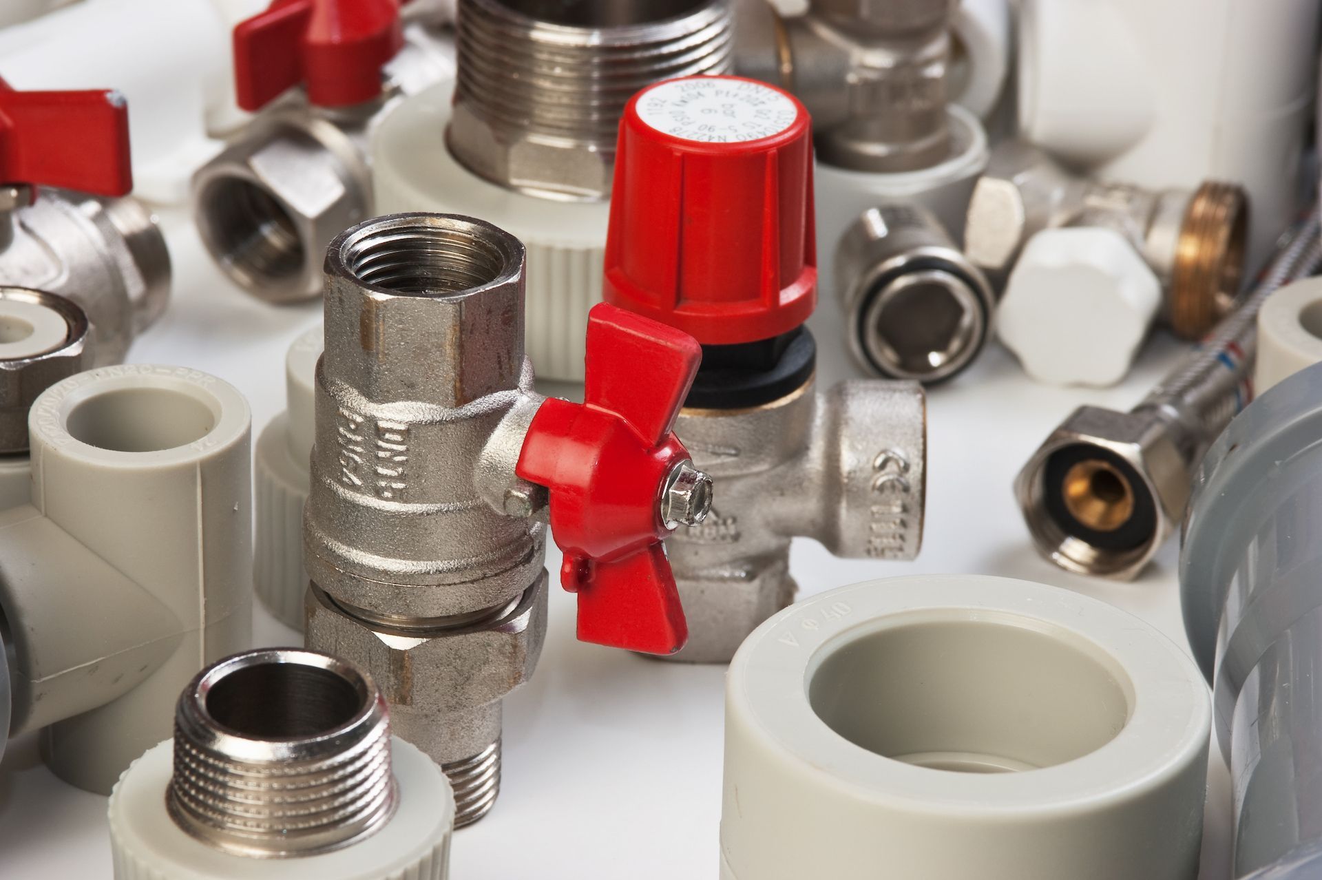 Plumbing fittings and valves in various sizes and materials, including red-handled valves.