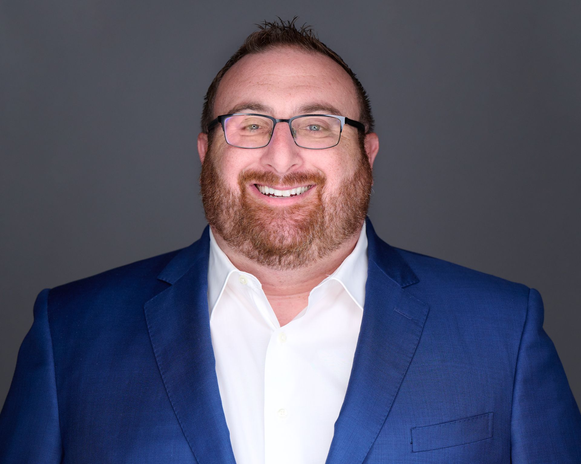 A bald man wearing glasses and a suit and tie is smiling for the camera.