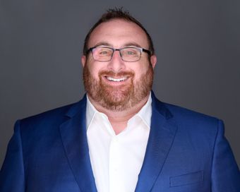 A bald man wearing glasses and a suit and tie is smiling for the camera.