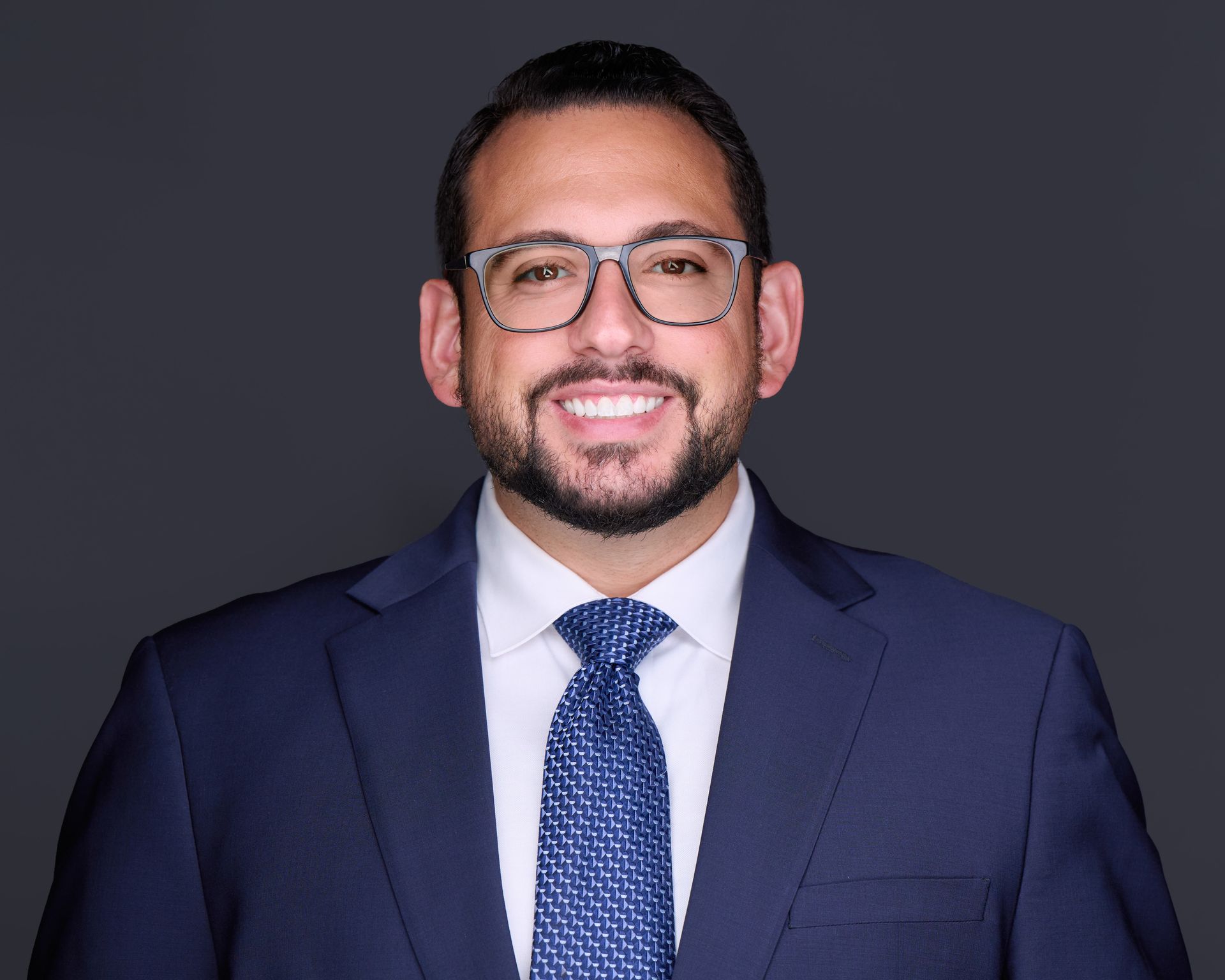 A bald man wearing glasses and a suit and tie is smiling for the camera.