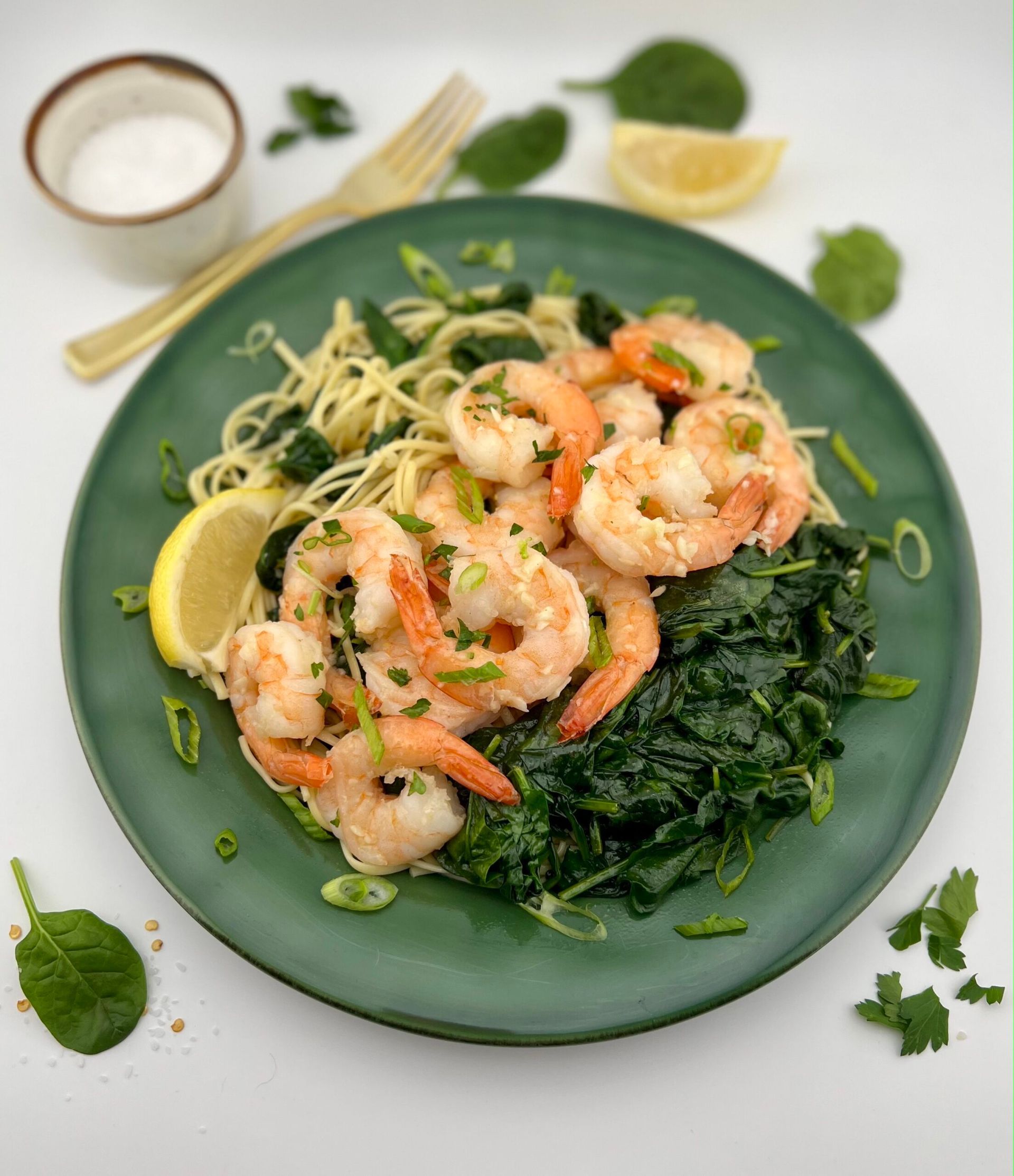 Shrimp scampi with pasta and spinach on a green plate, garnished with lemon and herbs.