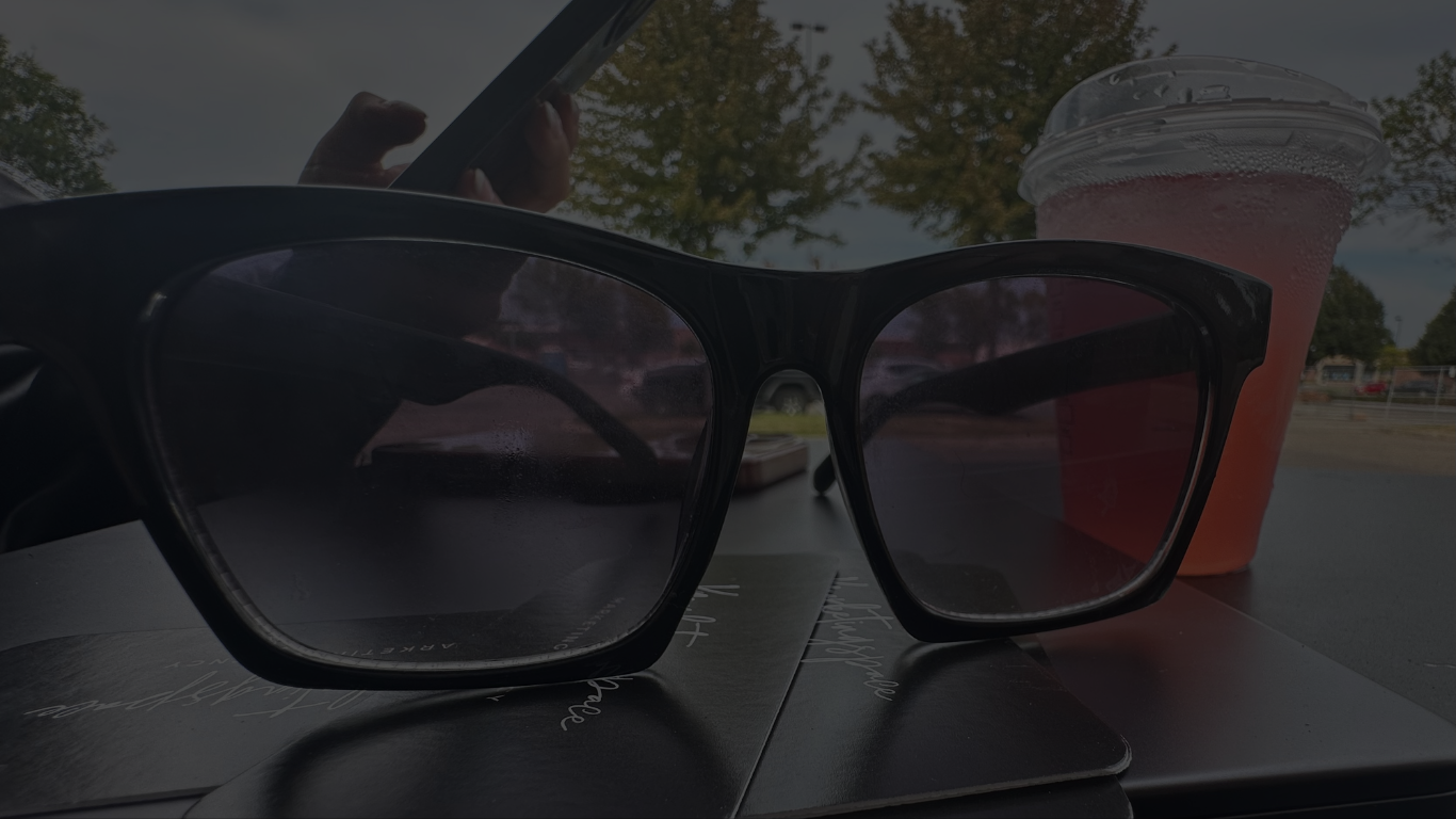 A pair of sunglasses is sitting on a table next to a cup of coffee.