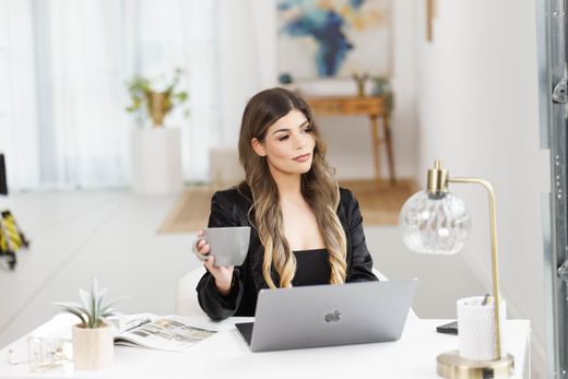 A woman is sitting at a desk with a laptop and a cup of coffee.