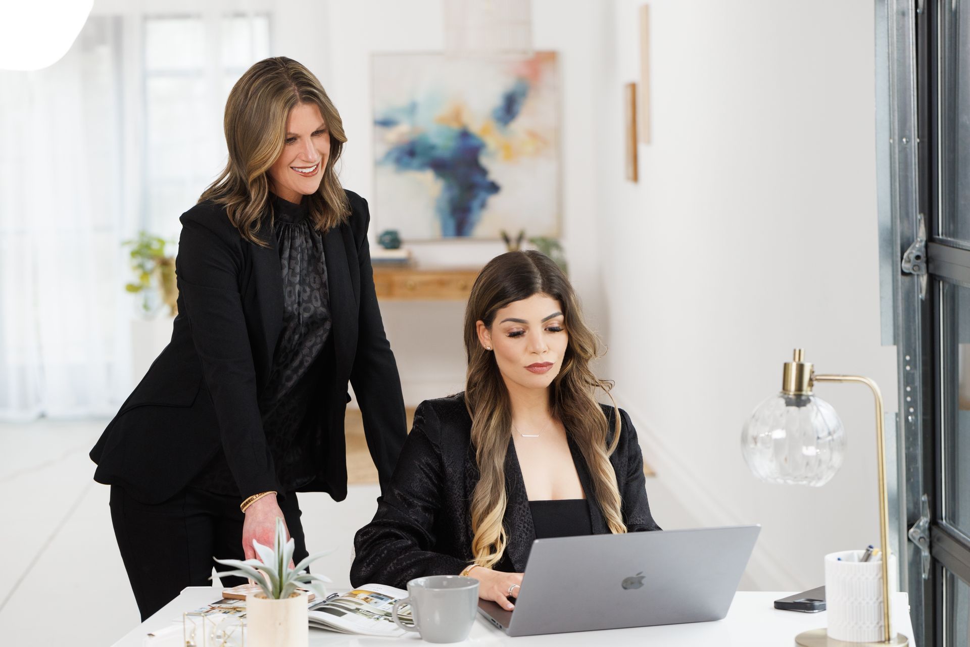 Two women are standing next to each other in front of a laptop computer.