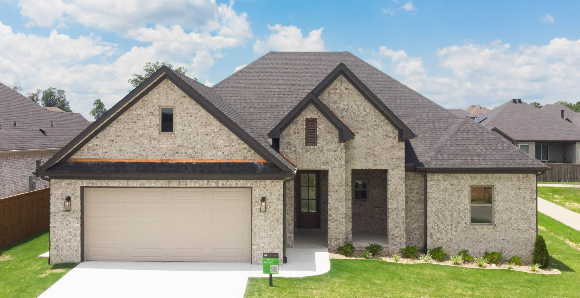 Simple custom home built by hines homes with dark brick and a white accent wall out front with a curved front porch