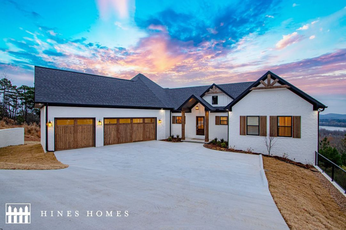 exterior of a home built by hines homes with a beautiful sunset behind it. the garage doors are wood and the brick is white