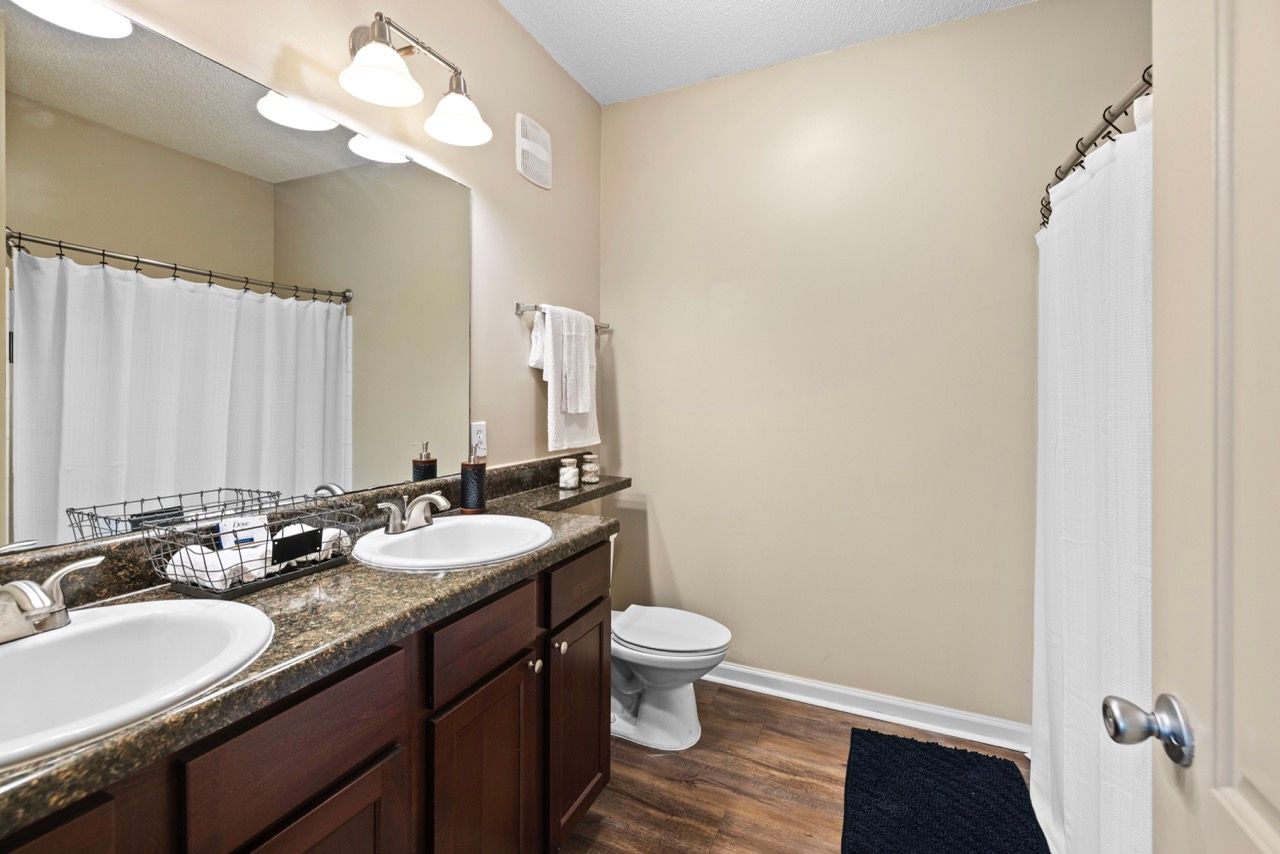 Bathroom with dual sinks, granite countertop, large mirror, and a shower with curtain.