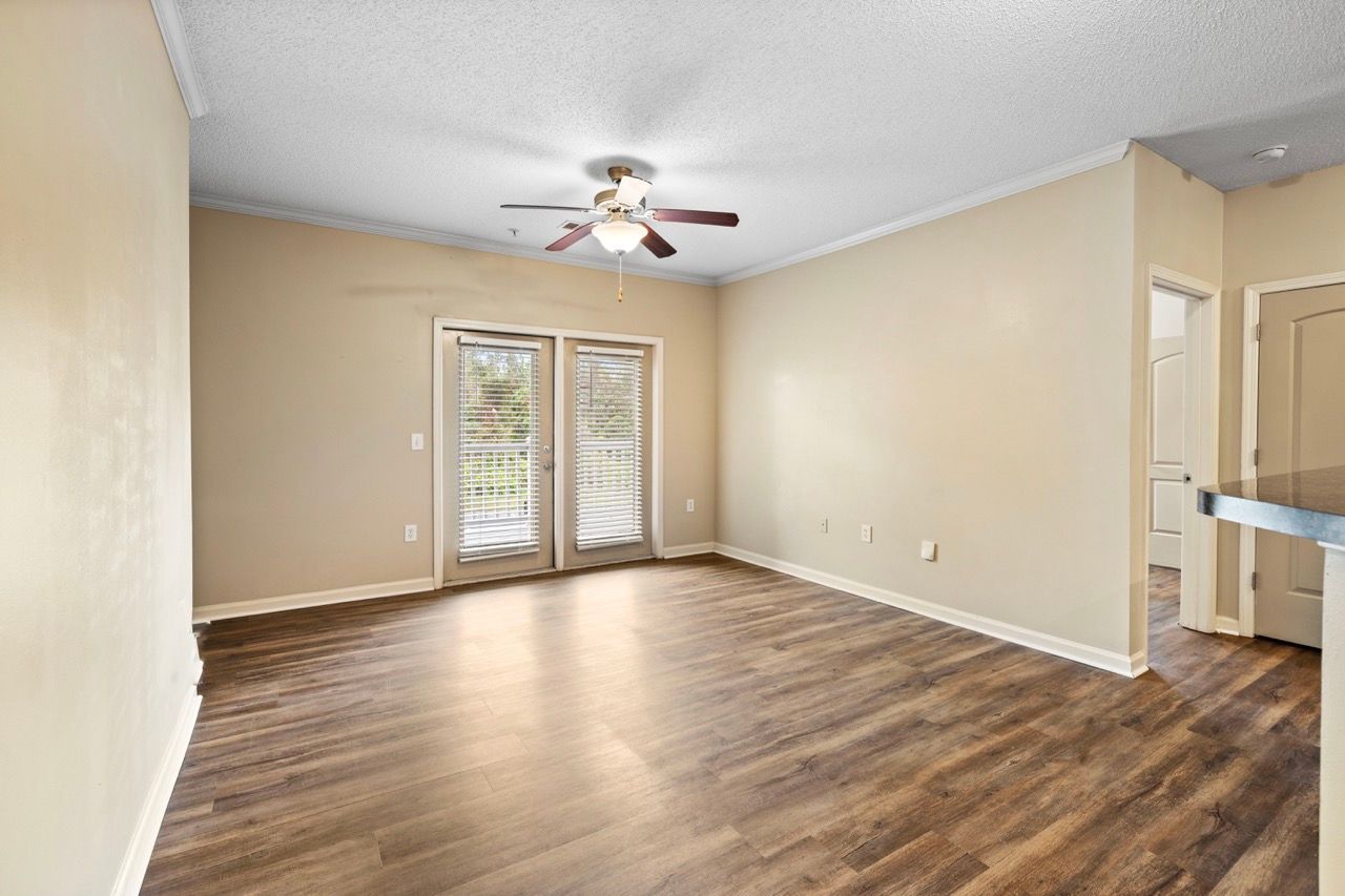 Empty living room in an apartment with wood-look flooring, beige walls, and a ceiling fan.