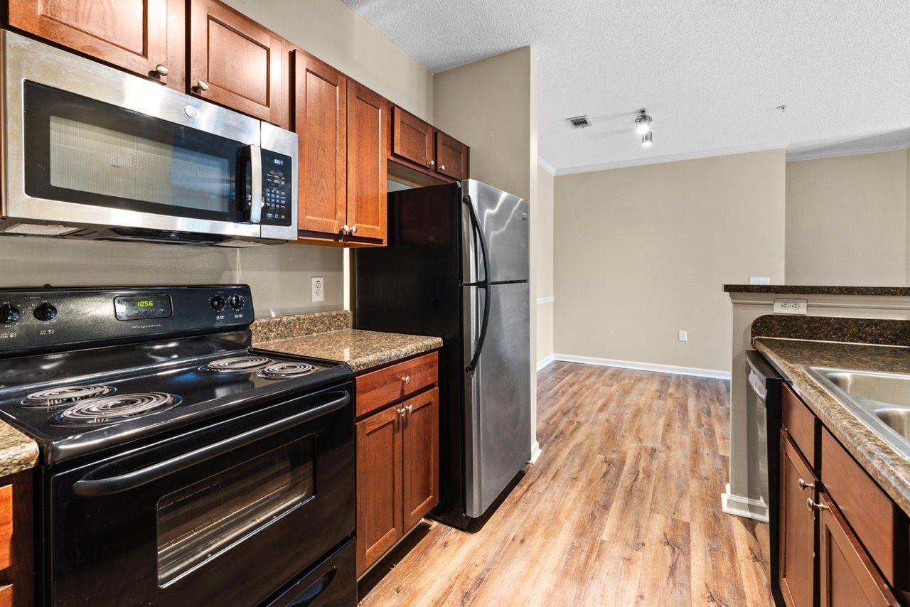 Modern apartment kitchen with stainless steel refrigerator, microwave, stove, granite countertops, and wood cabinets.