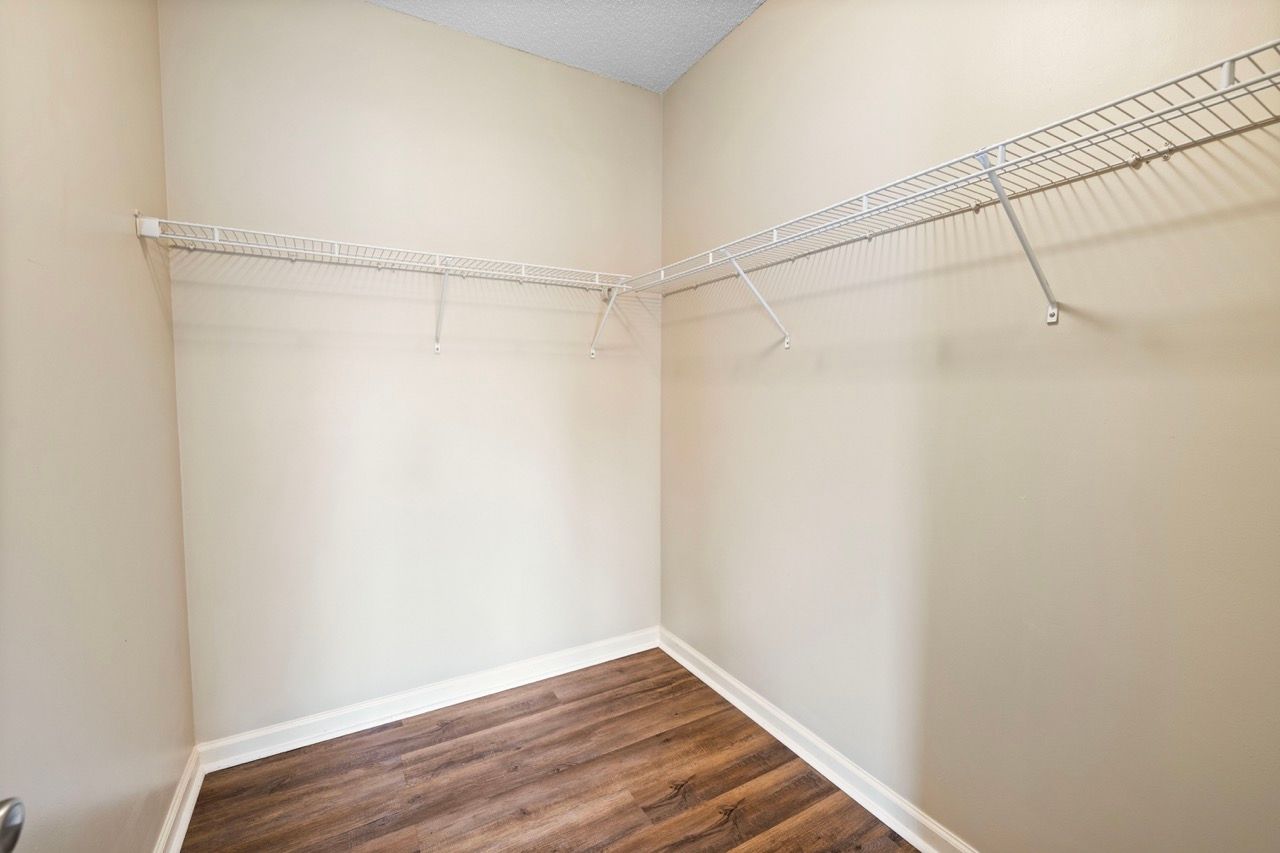 Walk-in closet with white wire shelving along two walls and wood-look flooring.