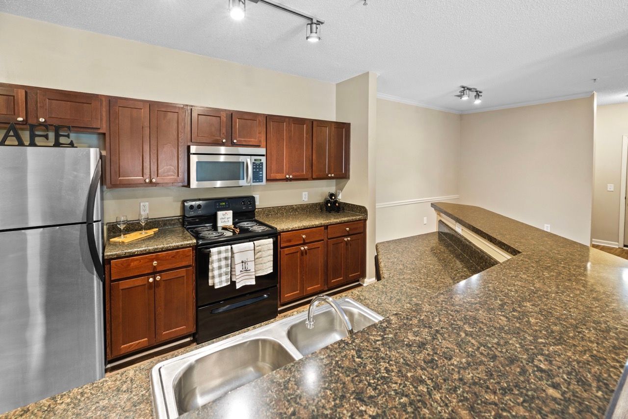 Kitchen in an apartment with granite countertops, dark wood cabinets, stainless steel refrigerator, stove, microwave, and double sink.