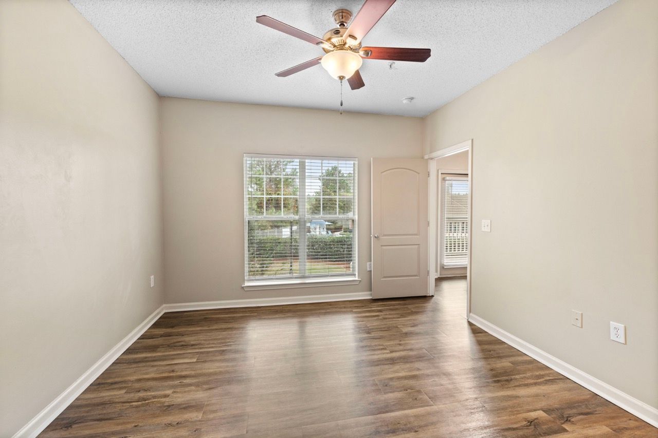 Empty living room with wood-look flooring, a window, ceiling fan, and doorway.