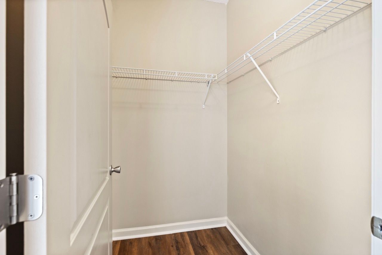 Empty walk-in closet with white wire shelves and wood-look flooring, seen from doorway.