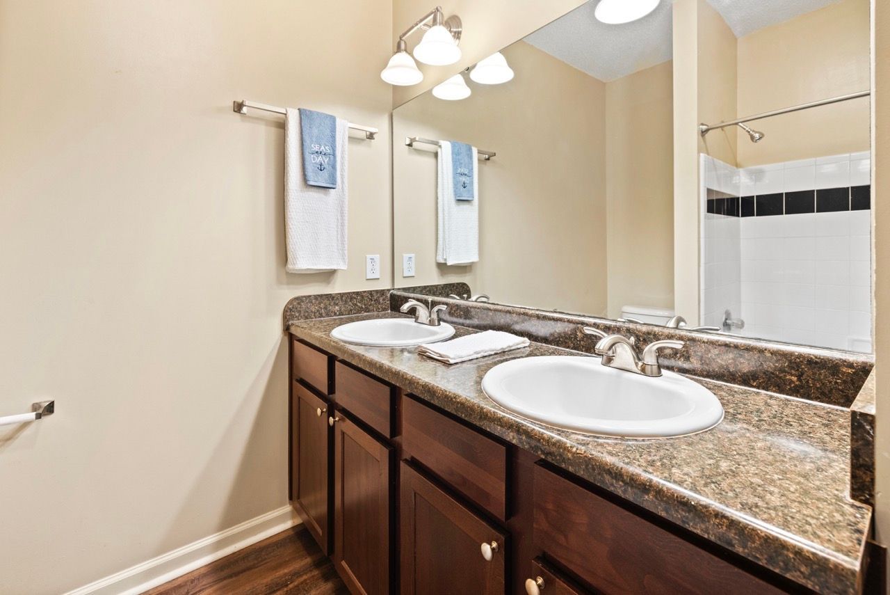 Double-sink bathroom vanity with granite countertop and a tiled shower.